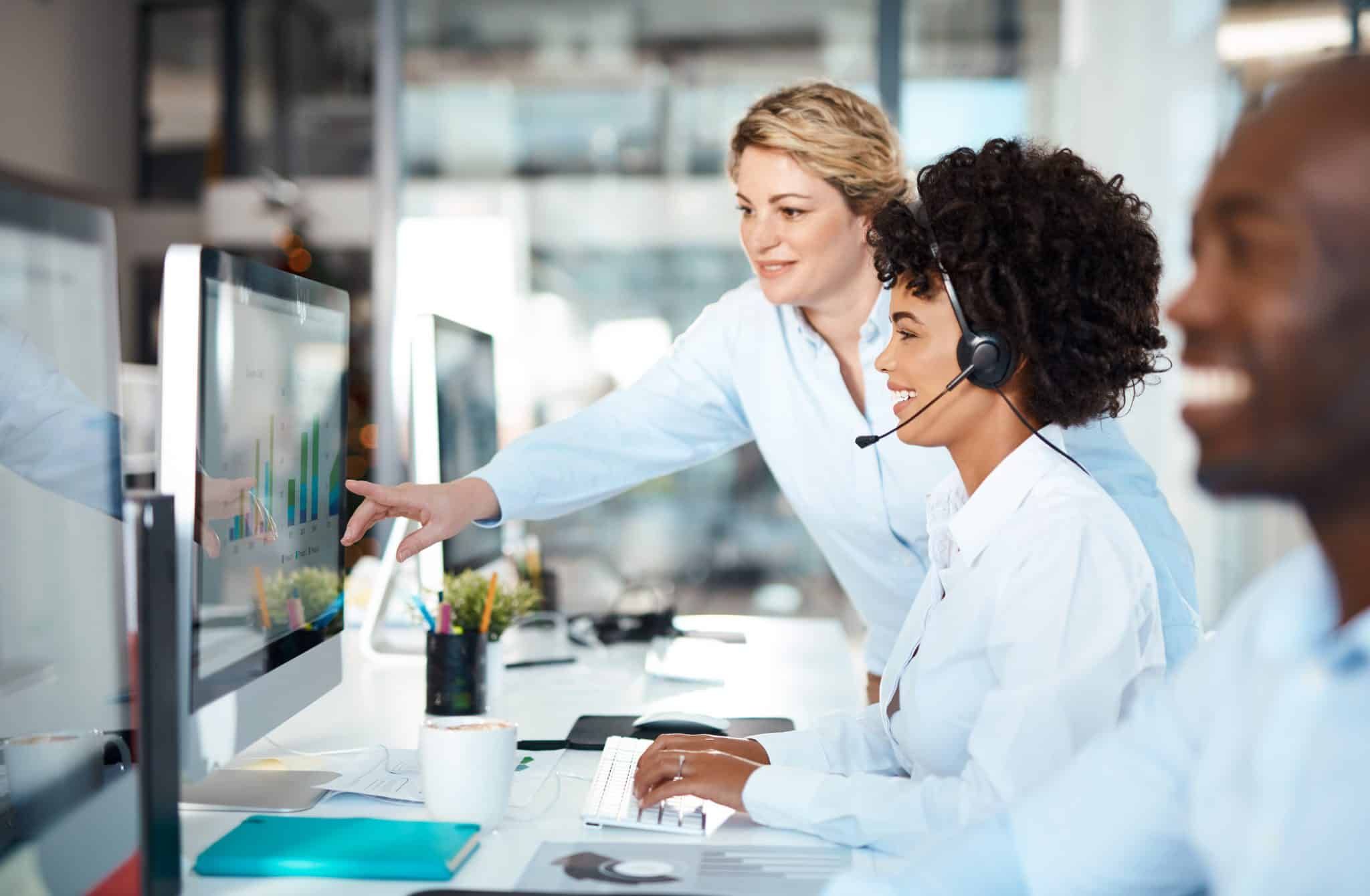 Intake specialist wearing a headset, smiling while a supervisor points to call data on screen